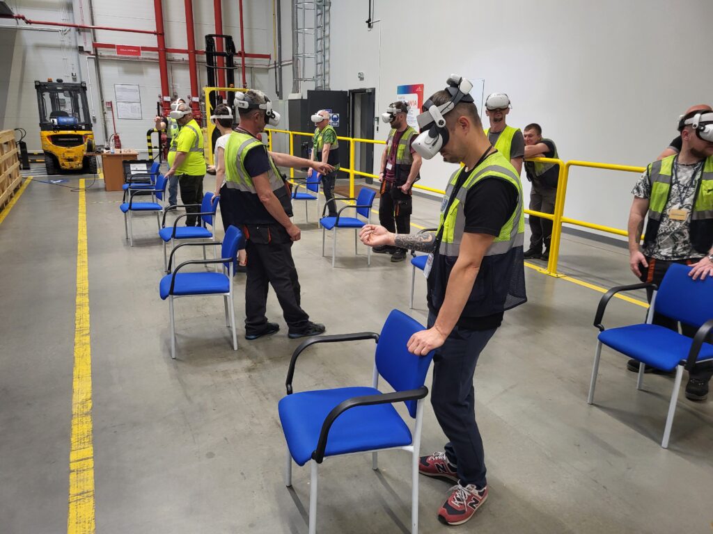 Dzień BHP – szkolenia VR dla dużych grup - ludzie na hali produkcyjnej grają w okularach VR